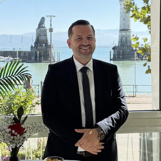 Lerch Businesswelten - Inspirationen an einem Tag Lächelnder Mann im Anzug vor einem großen Fenster mit Blick auf das Wasser