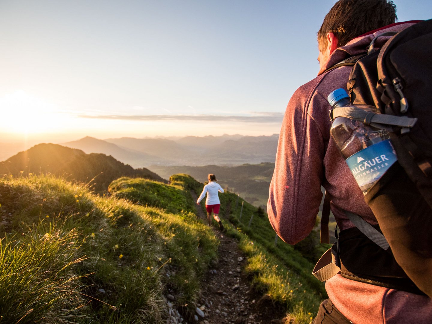 Hotel Das Weitblick Allgäu | Unsere Lieferanten Wanderer mit Rucksack auf einem Bergpfad bei Sonnenuntergang
