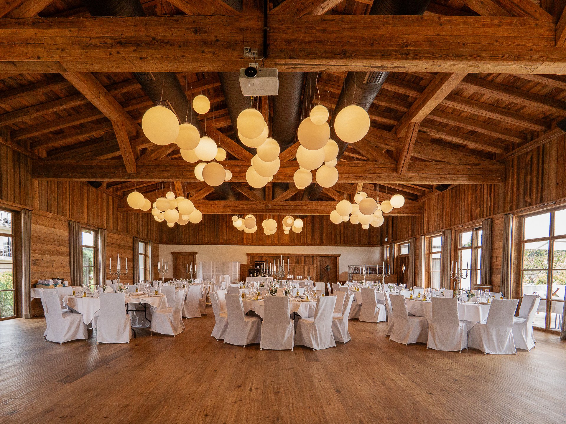 Hotel Weitblick Allgäu | Heiraten & Feiern in stilvollem Ambiente Großer rustikaler Bankettsaal mit runden Tischen und weißen Stuhlbezügen