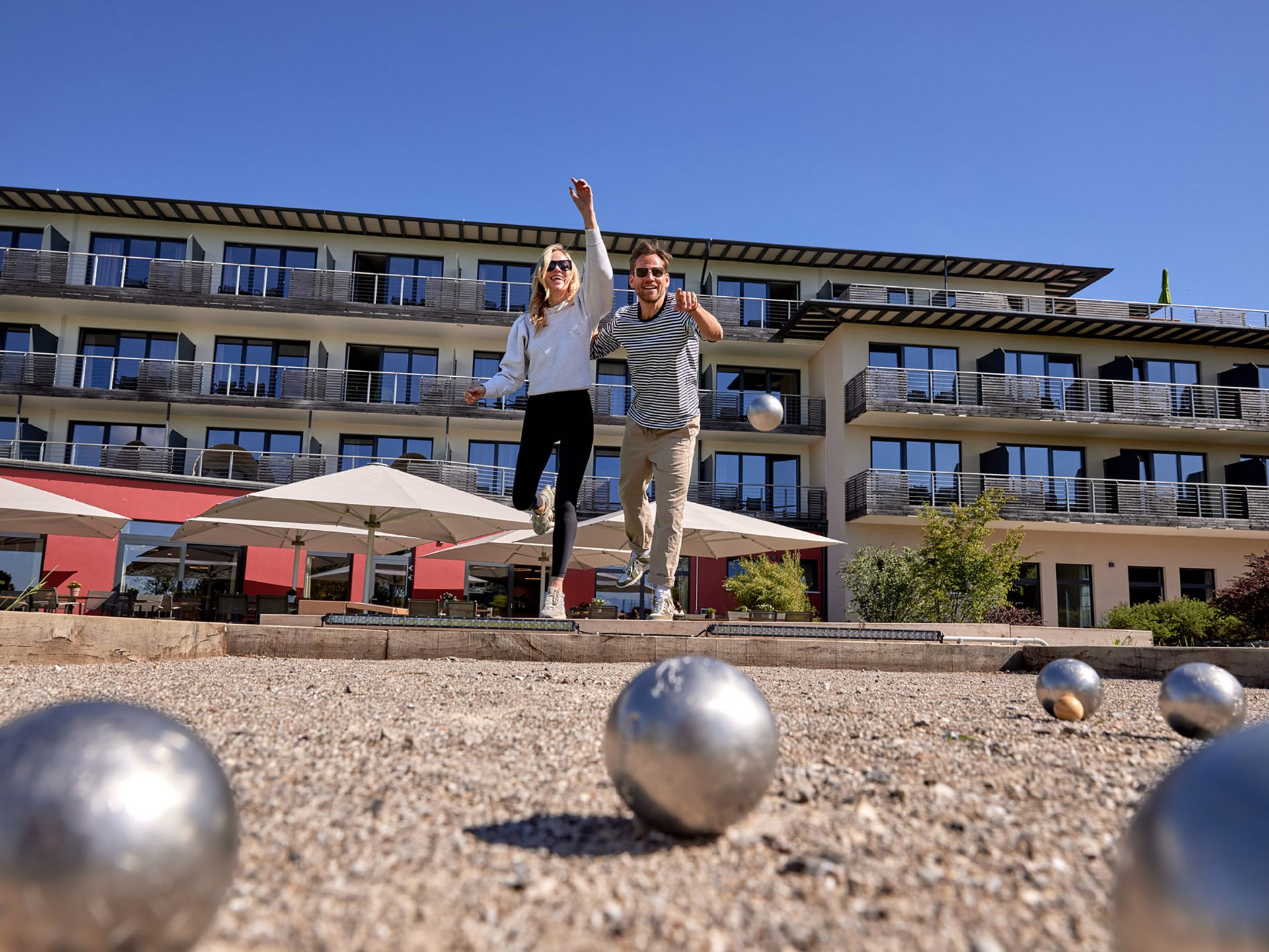 Teambildung & Gruppenevents im Allgäu Paar spielt Boule vor einem modernen Hotel bei sonnigem Wetter