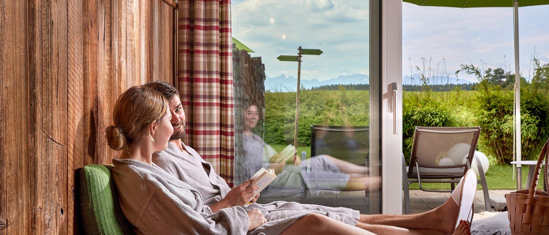 Paar in Bademänteln entspannt sich drinnen mit Blick auf Terrasse und Garten