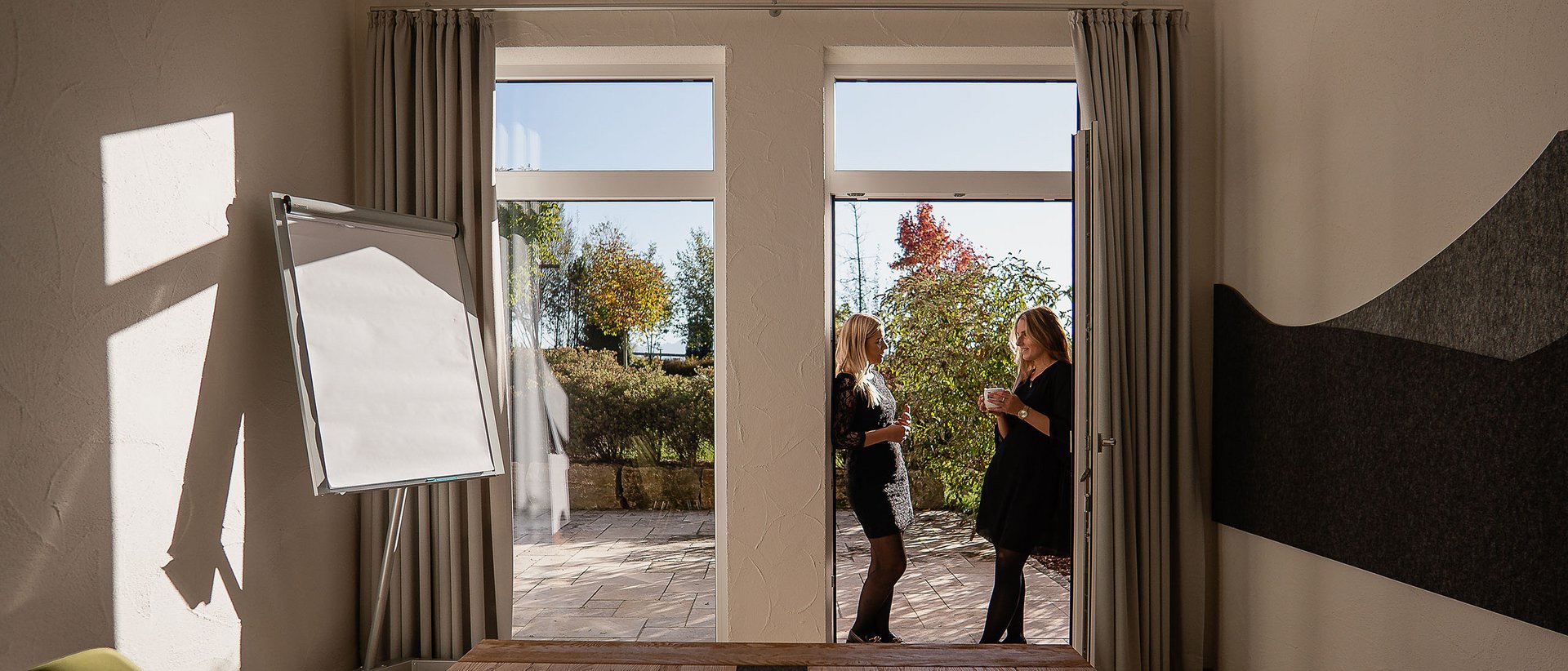 7557 Zwei Frauen unterhalten sich draußen vor einem Raum mit Flipchart und Holztisch