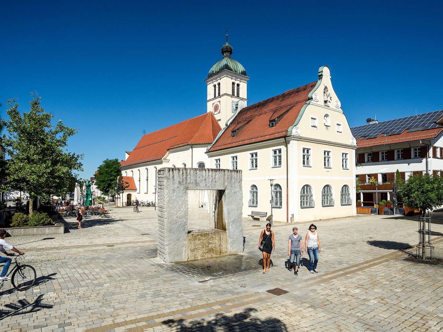 Autofrei in Das Weitblick Allgäu reisen Historisches Gebäude mit rotem Dach und Uhrturm an sonnigem Platz mit Brunnen