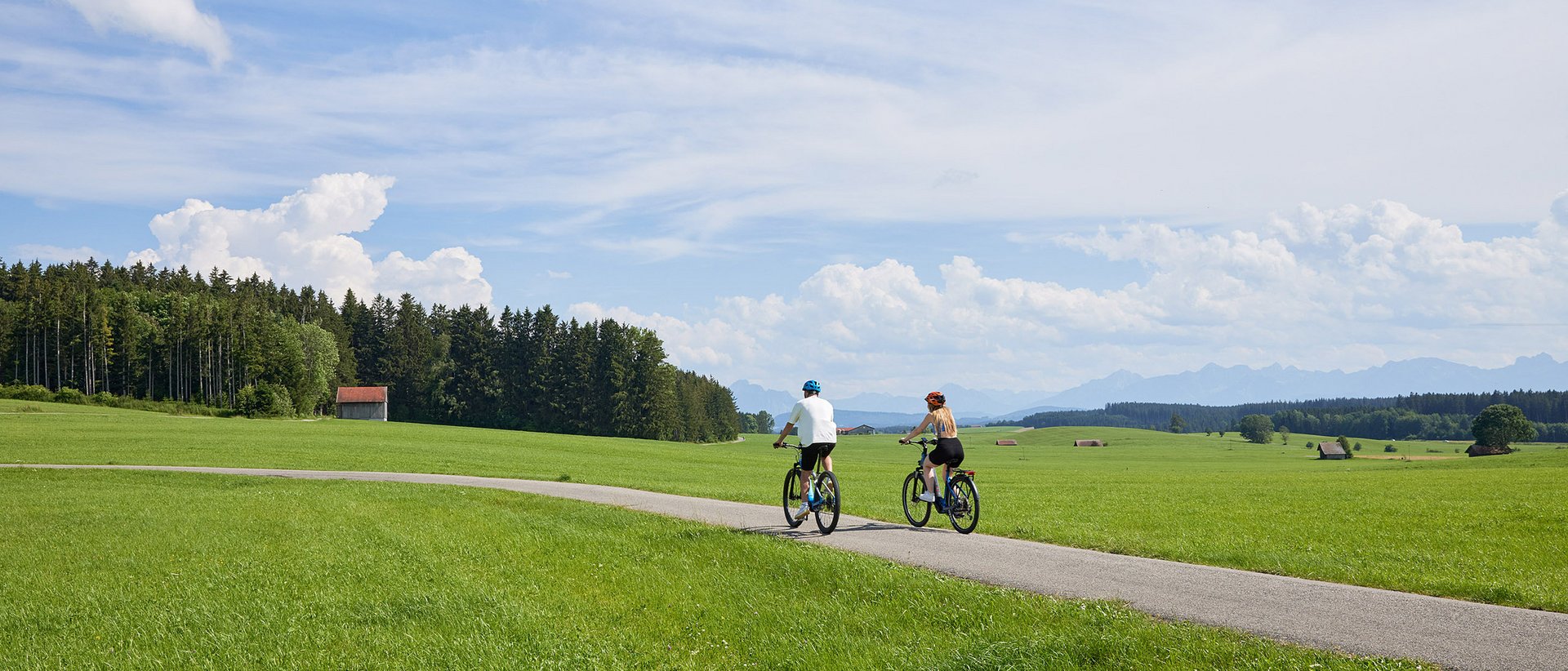 Radweg Leutkirch-Isny Zwei Radfahrer auf einem Weg durch grüne Wiesen unter blauem Himmel