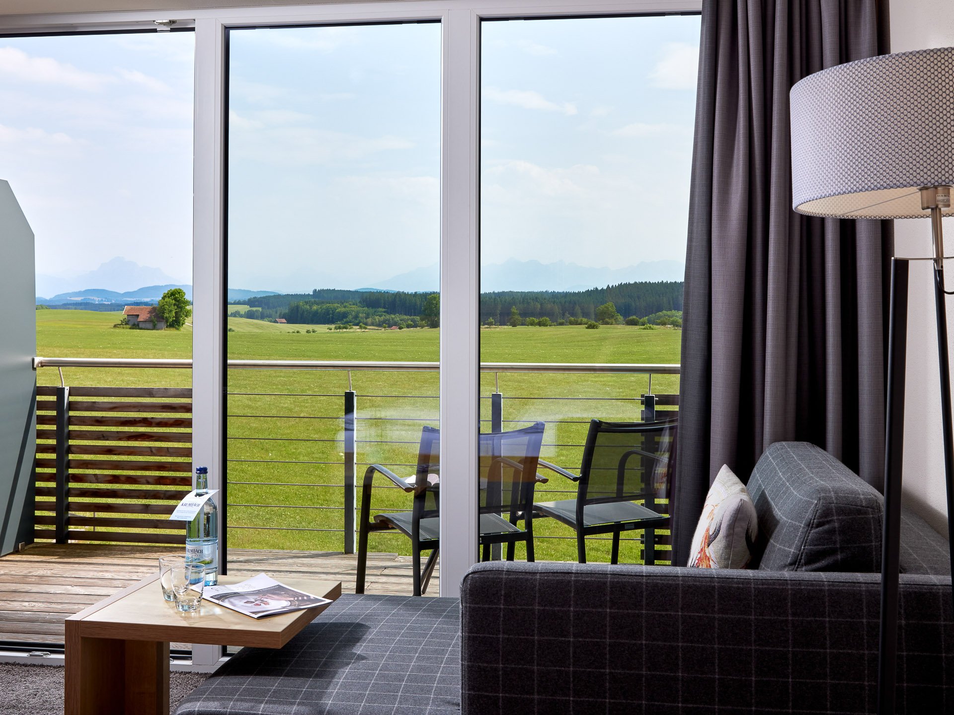 7793 Modernes Wohnzimmer mit Sofa, Stehlampe und Balkon mit Blick auf grüne Wiesen