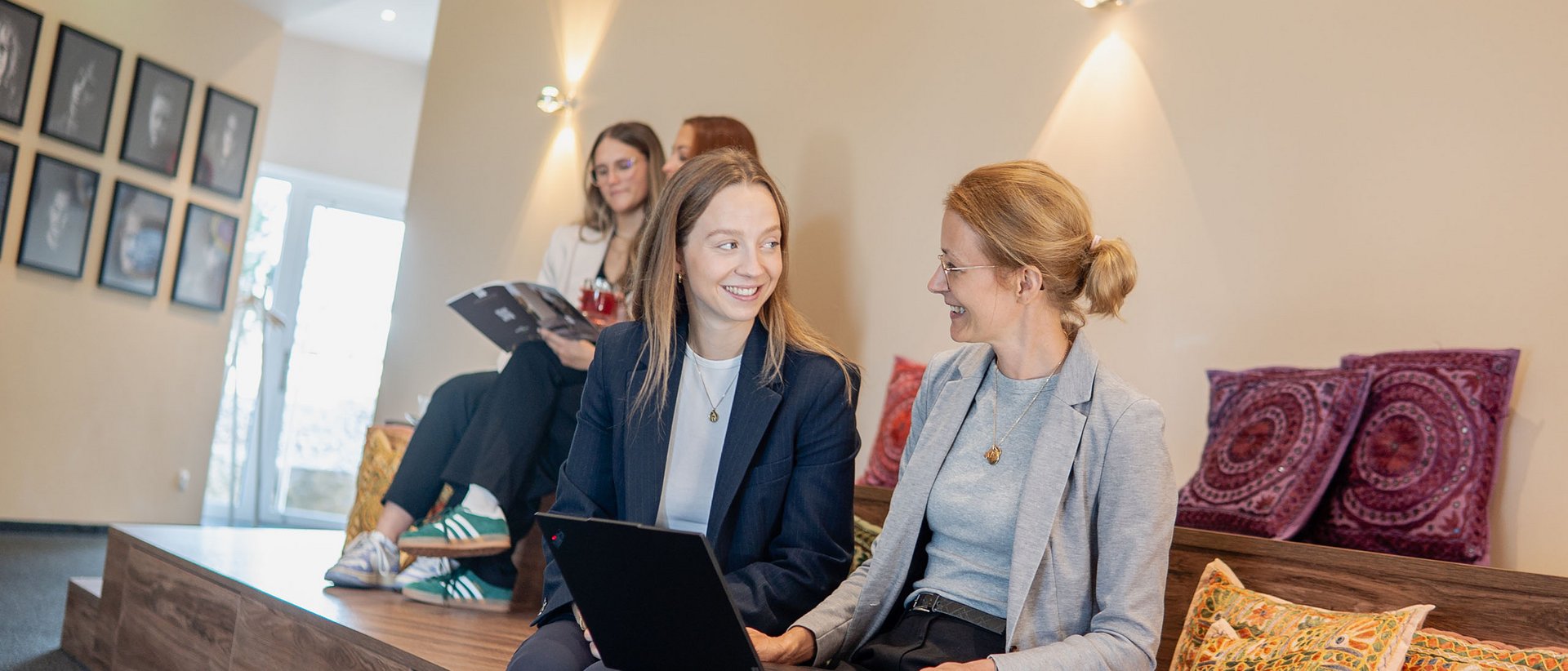 Lerch Businesswelten - Inspirationen an einem Tag Zwei Frauen sitzen mit Laptop auf einer Holzbank mit bunten Kissen im modernen Raum