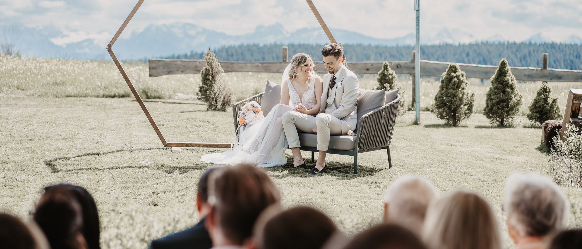 Die wichtigsten Informationen im Überblick Brautpaar sitzt auf Sofa vor sechseckigem Rahmen bei Outdoor-Hochzeit