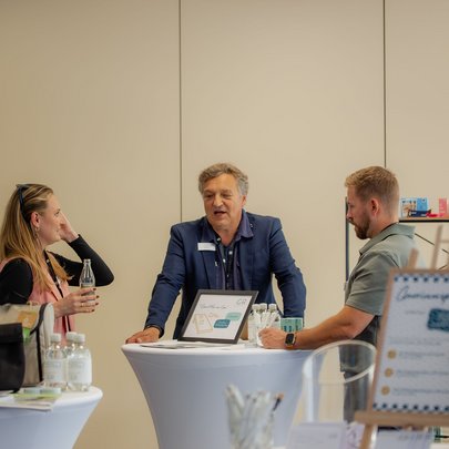 Lerch Businesswelten - Inspirationen an einem Tag Drei Personen im Gespräch an einem Messestand mit Getränken und Präsentationsmaterial
